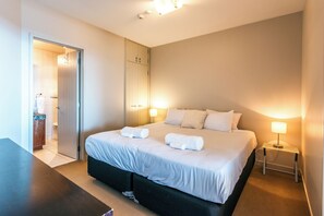 A hotel room with a bed, bedside lamps, a desk, and a wardrobe. - Sanctuary On The Beach (Waiheke Island)