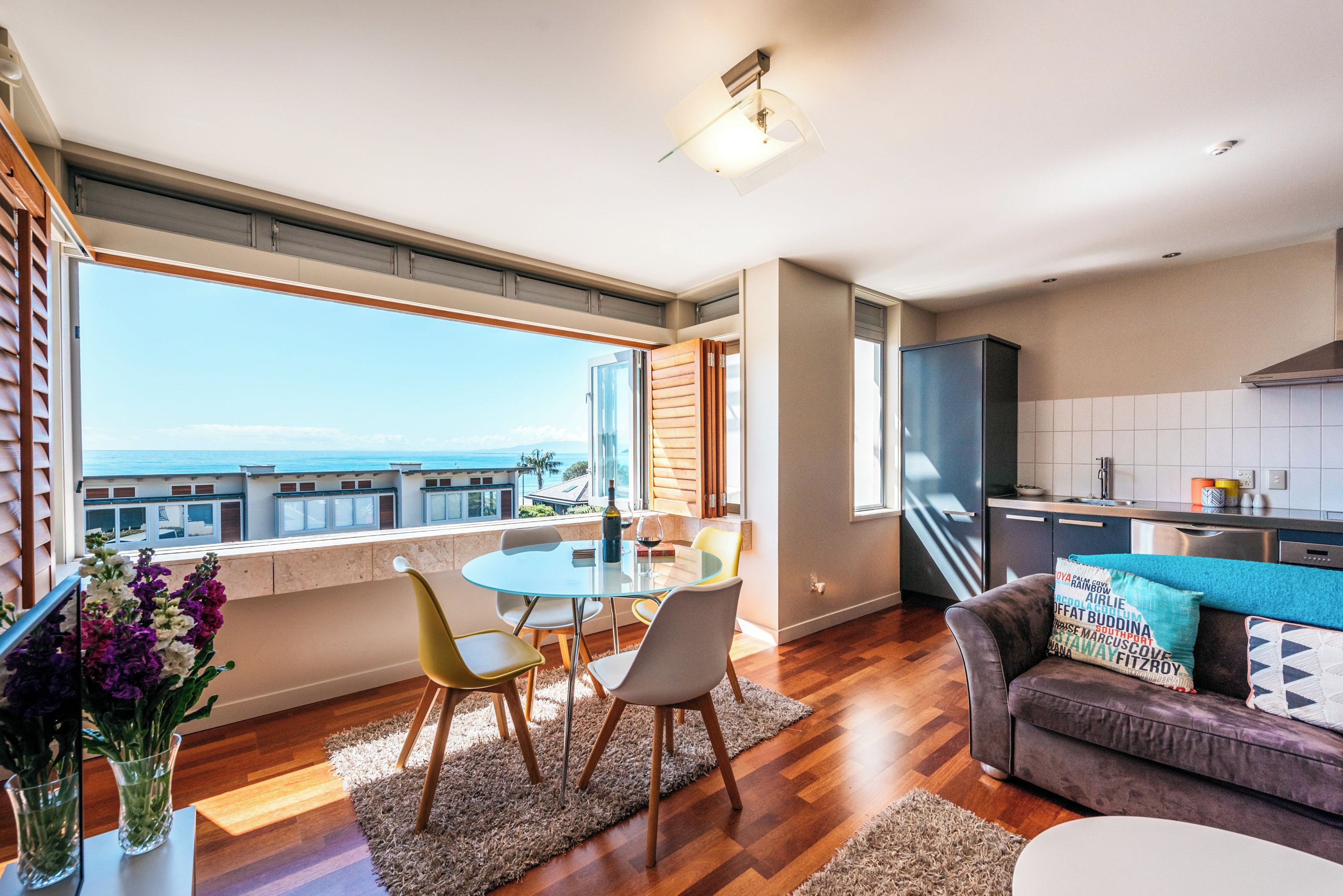 A modern living space with a dining area, kitchen, and a large window offering a view of the sea.