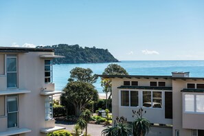 A coastal residential area with buildings overlooking the sea, featuring balconies and a view of a distant hill. - Sanctuary On The Beach (Waiheke Island)