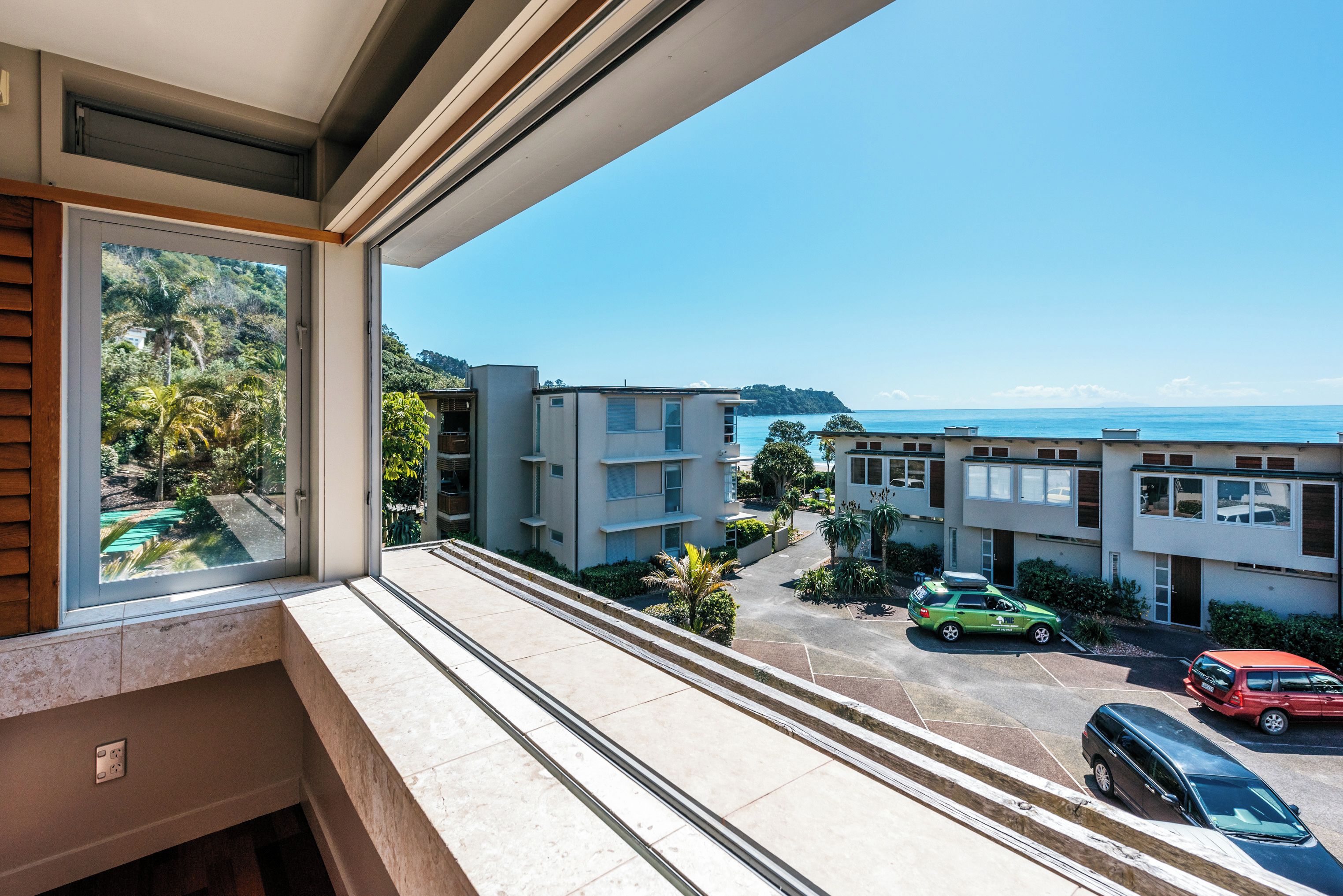 A residential building with a view of the ocean and parked cars.