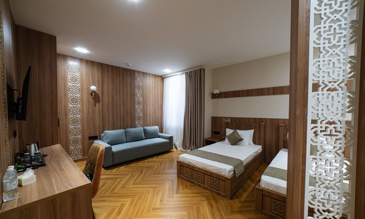Habitación de hotel con piso de madera, una cama con cabecera, un sofá, un escritorio con silla y un panel decorativo.