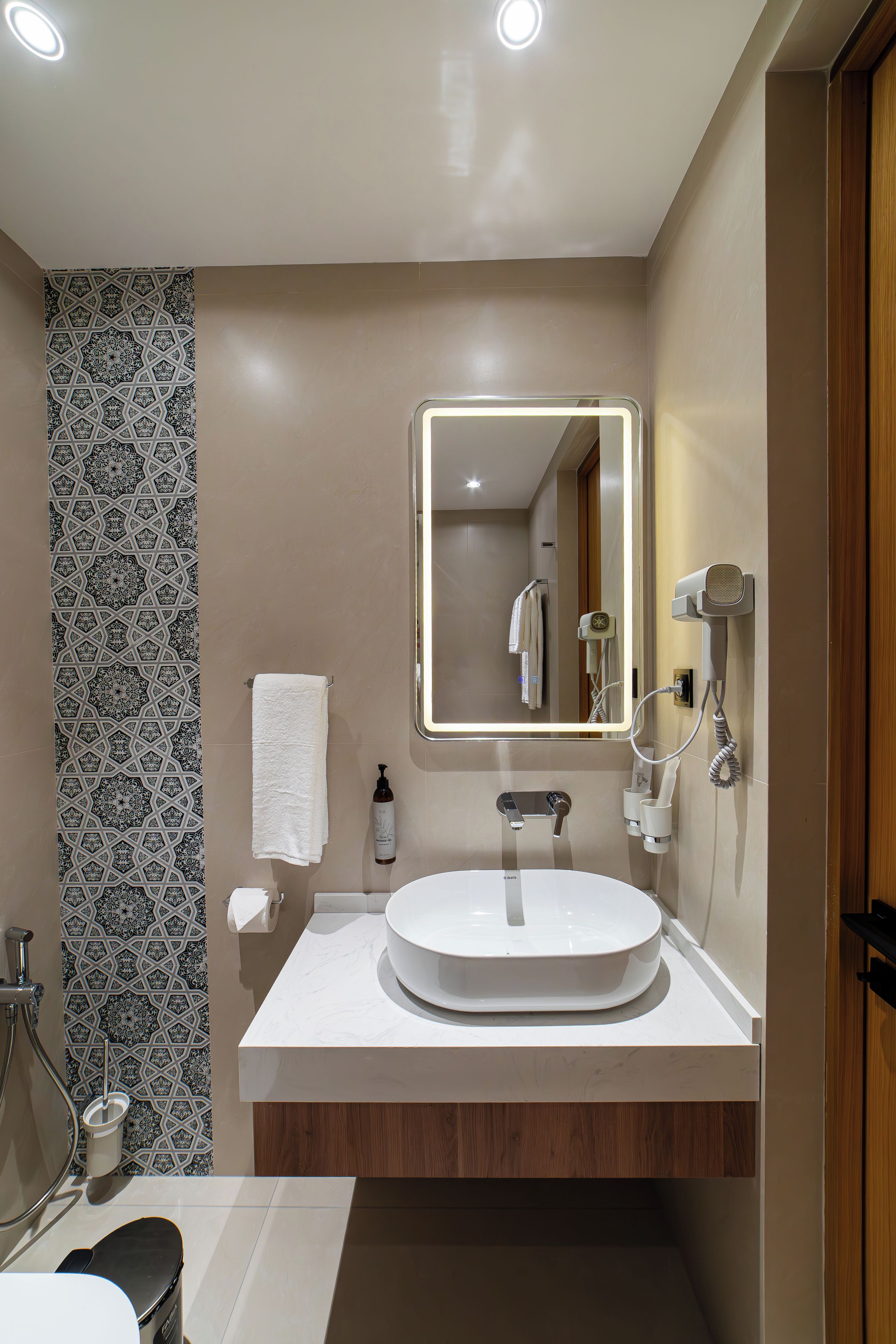 Un bagno moderno con un lavandino rotondo, uno specchio con illuminazione, un porta asciugamani, una zona doccia e un WC.