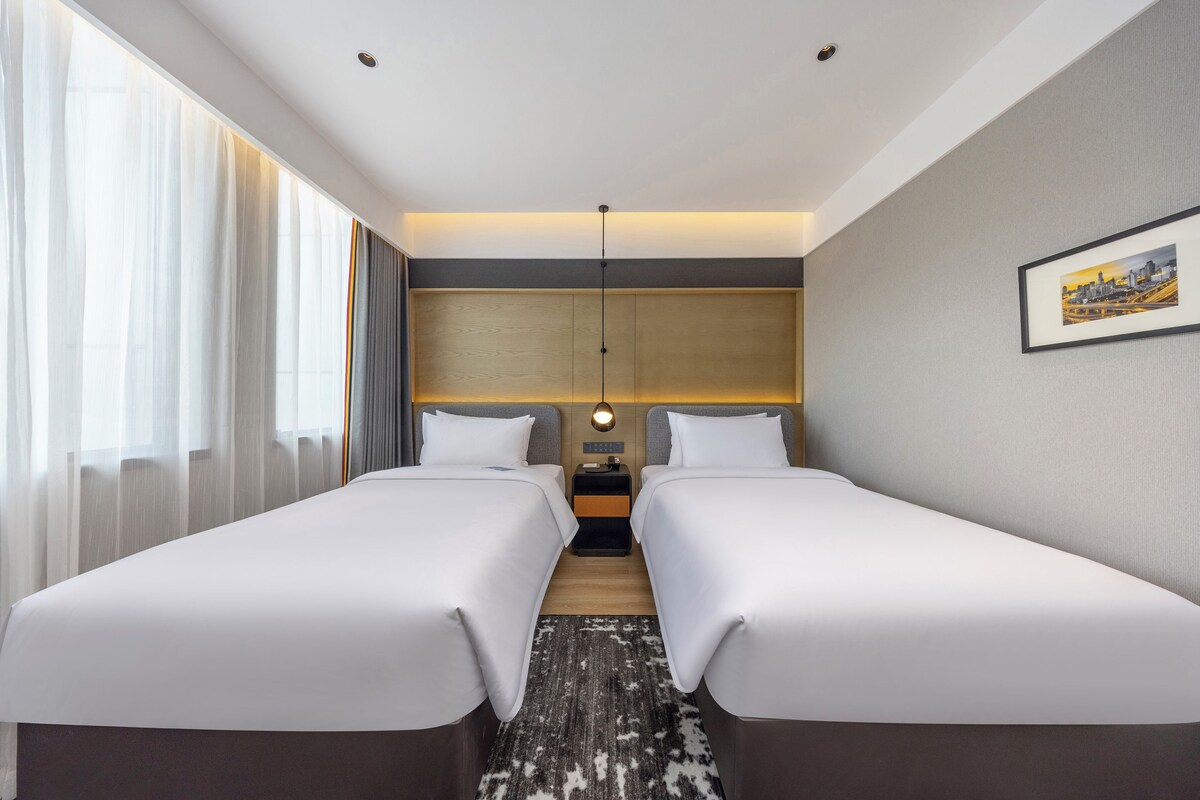 Een hotelkamer met twee bedden, een nachtkastje, een lamp en een ingelijst schilderij aan de muur.