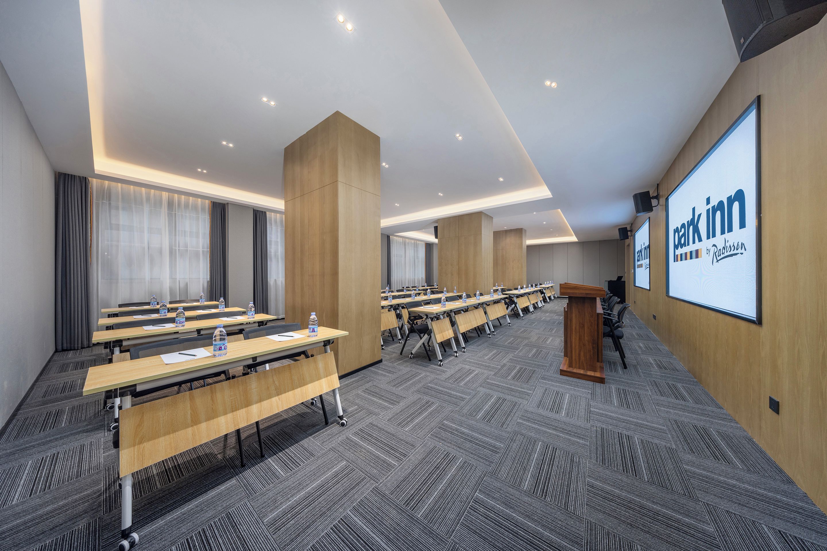 A conference room with multiple tables, chairs, and a large screen displaying the brand name.