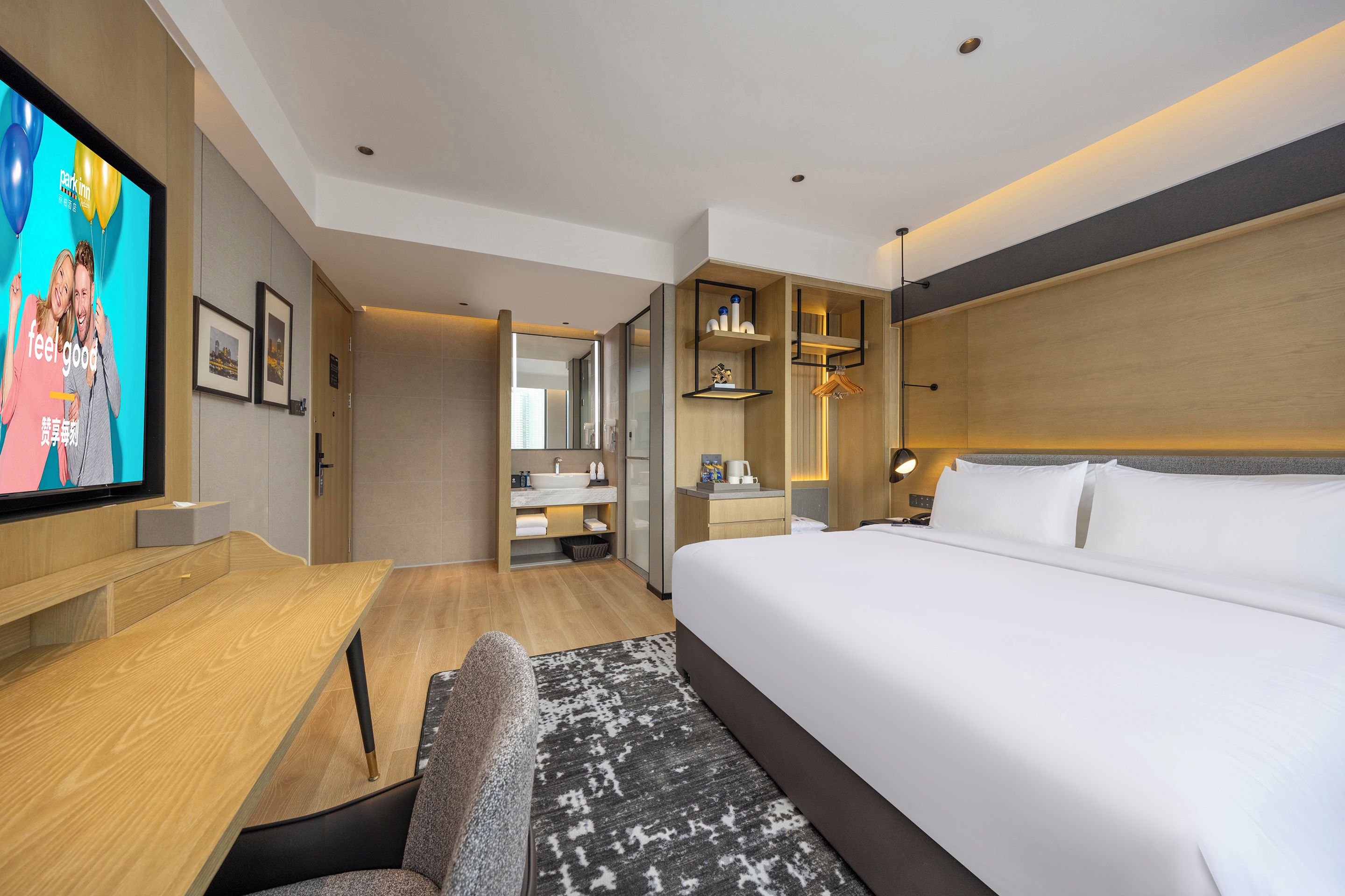 A modern hotel room with a large bed, a desk, a television, and a bathroom with a mirror and sink.