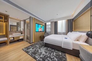 Een moderne hotelkamer met een groot bed, een badkamer met wastafel, een televisie en uitzicht op de stad.