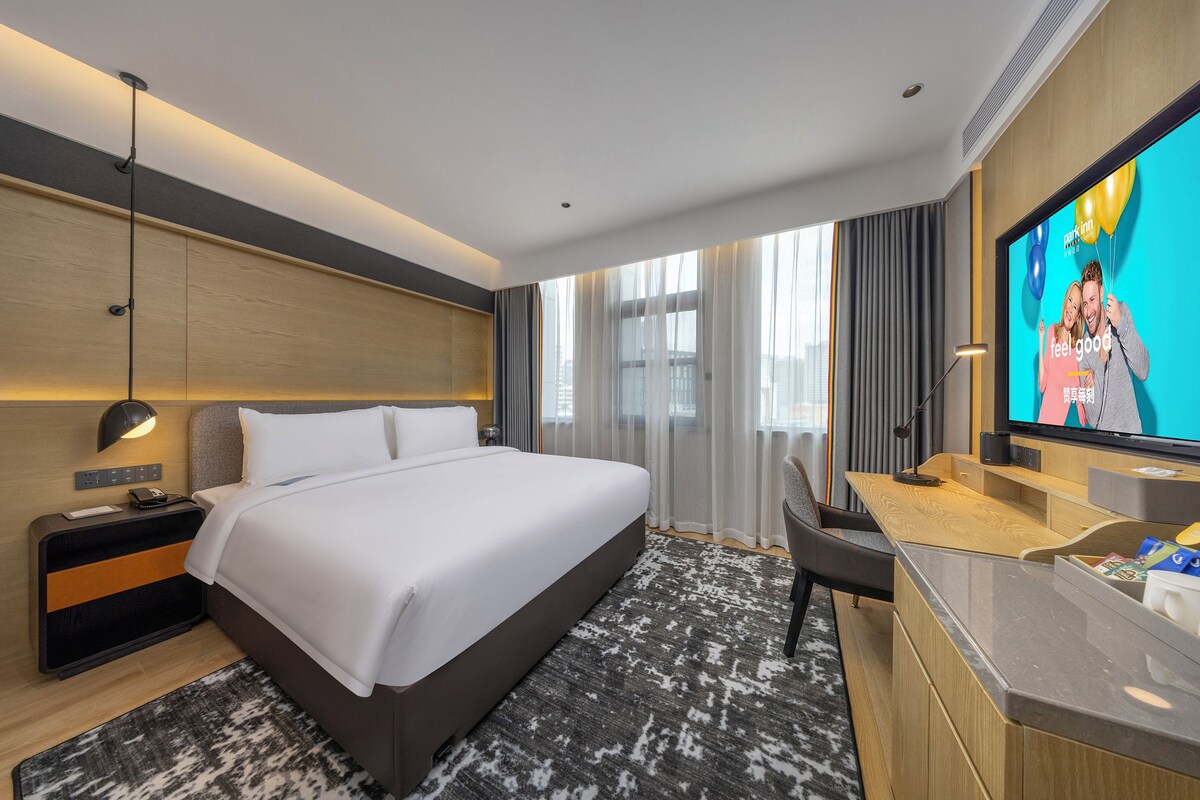 Een moderne hotelkamer met een groot bed, een bureau, een televisie en uitzicht op de stad.