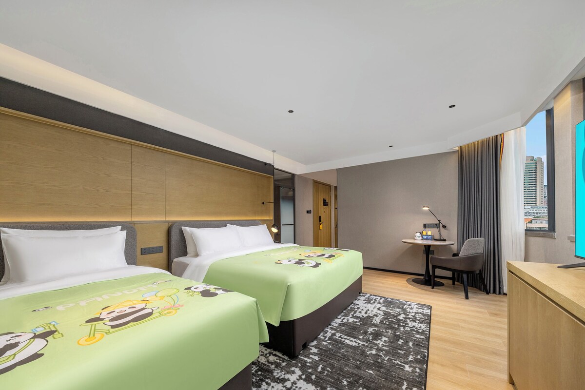 Een hotelkamer met twee bedden, een bureau, een stoel en een groot raam.