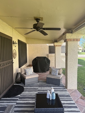 Une terrasse extérieure aménagée avec des meubles en osier, un ventilateur de plafond et un barbecue couvert.