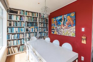 Ein Zimmer mit einem großen Bücherregal, einem Esstisch mit Stühlen und einem farbenfrohen Bild an der Wand.