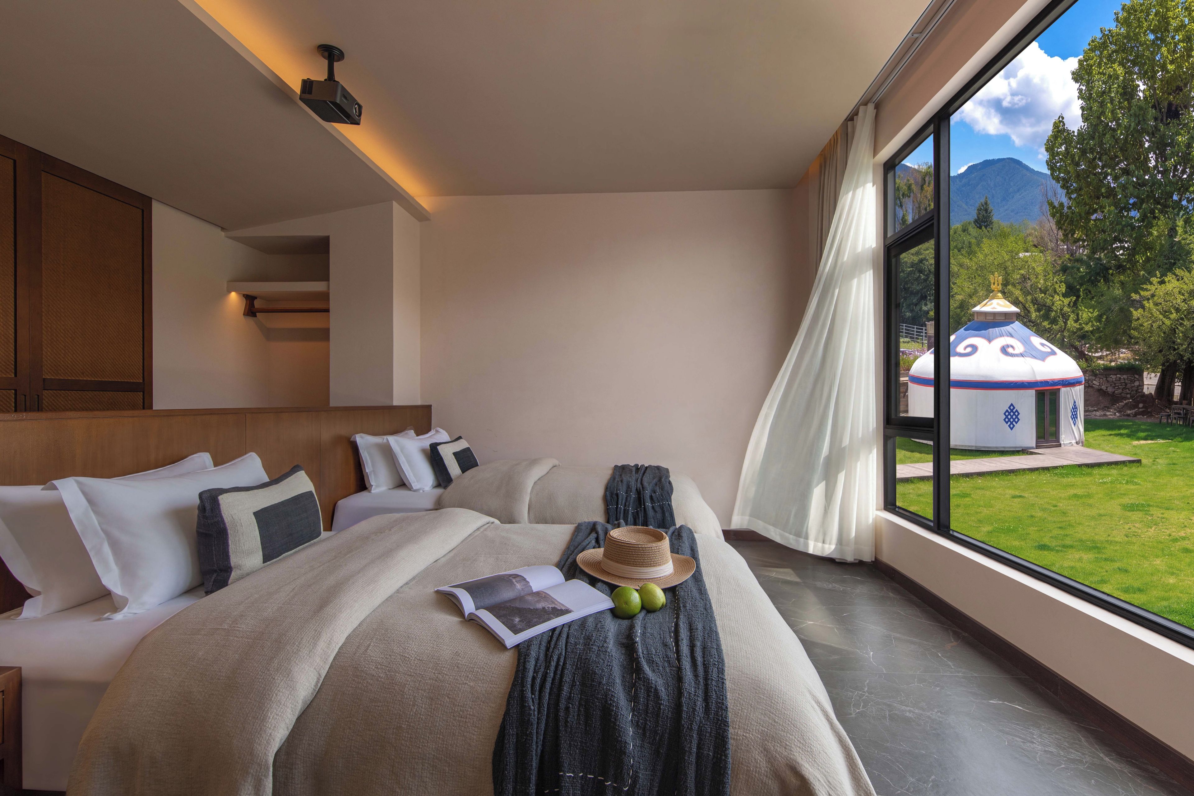 A modern bedroom with a large bed, a reading area, and a view of a mountain and a traditional building.