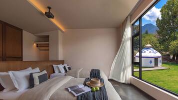 A modern bedroom with a large bed, a reading area, and a view of a mountain and a traditional building.