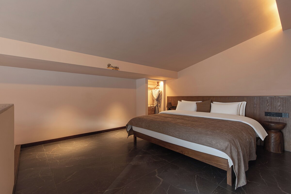 Un dormitorio con una cama, una mesita de noche, una lámpara de pared y un cartel sobre la cama.