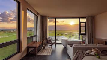 A modern hotel room with a large window offering a view of a green landscape and mountains.