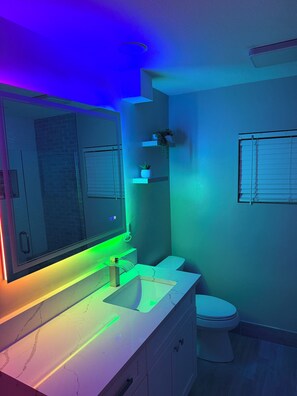 A bathroom with a modern design, featuring a large mirror, a white sink, and a toilet. - Stunning 4-Bedroom Riverfront Retreat with Private Hot Tub & Heated Pool! (Cape Coral)