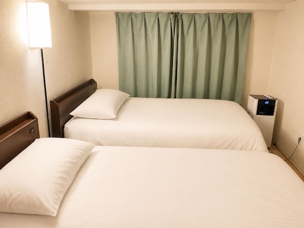 Ein Hotelzimmer mit zwei Betten, einem Nachttisch, einer Lampe, einer digitalen Uhr und einem Vorhang.