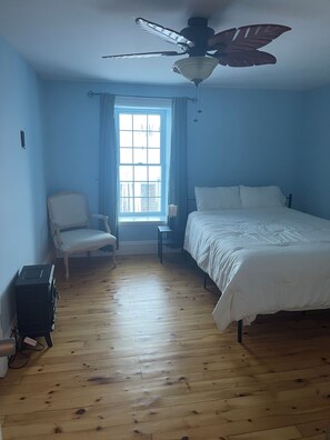 Ein Schlafzimmer mit einem Bett, einem Sessel, einem Schreibtisch und einem Deckenventilator.