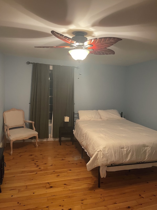 A bedroom with a bed, a chair, a desk, a ceiling fan, and a window with curtains.