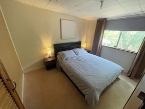 A bedroom with a bed, two bedside tables with lamps, a window with curtains, and a ceiling fan.