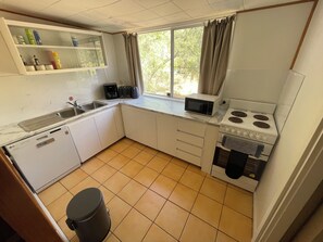 A compact kitchen with a sink, microwave, stove, and a window with curtains.