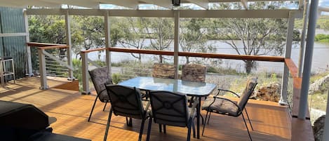 A covered outdoor area with a table and chairs, a grill, and a view of a body of water.