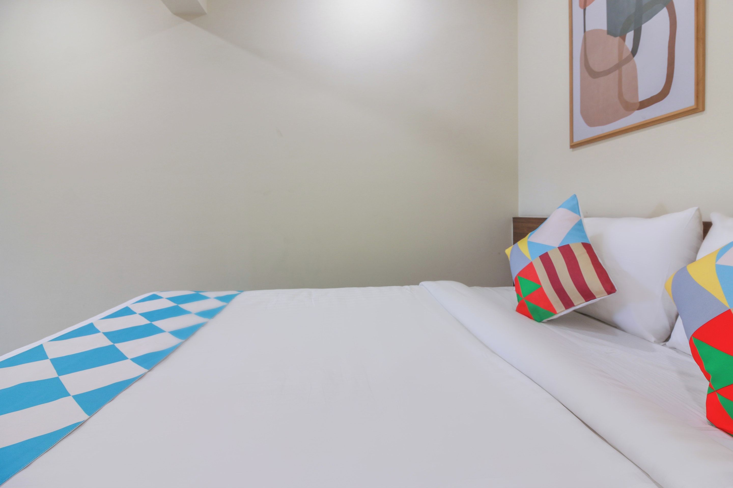 Una cama con edredón blanco y una manta azul y blanca a cuadros. Hay almohadas con diseños geométricos.