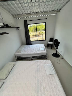 A room with a bed, a chair, a standing fan, and a window with a view of trees. - New Listing (Tolima)