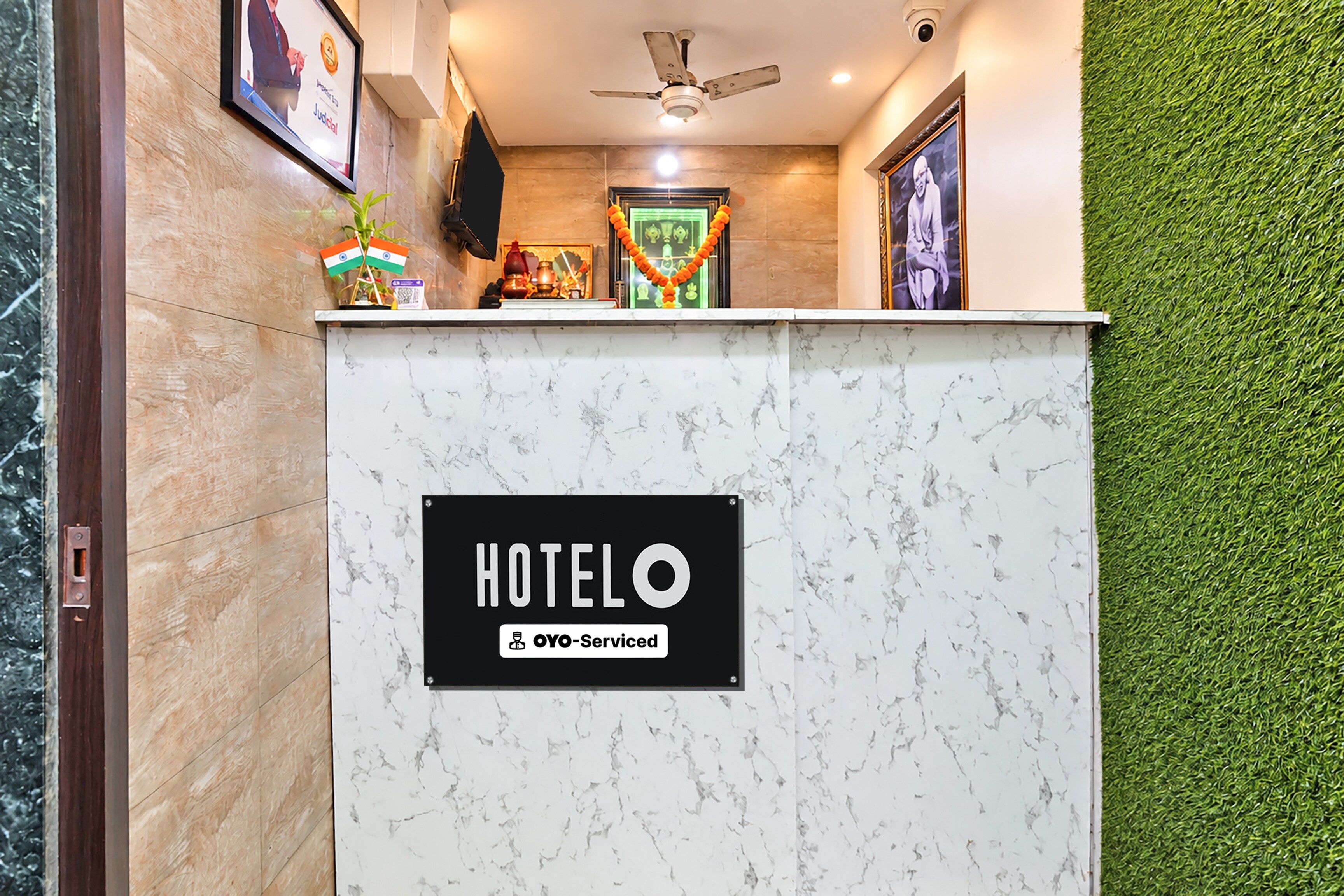 A hotel reception desk with a marble top, a sign indicating it is serviced by OYO, and a ceiling fan above.