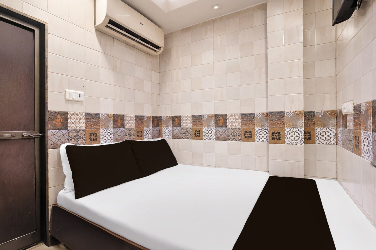 A hotel room with a bed, a door, an air conditioning unit, and patterned wall tiles.