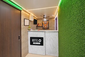 A hotel reception area with a marble counter, a ceiling fan, and a green wall. - HOTEL O CU LODGING (Mumbai)