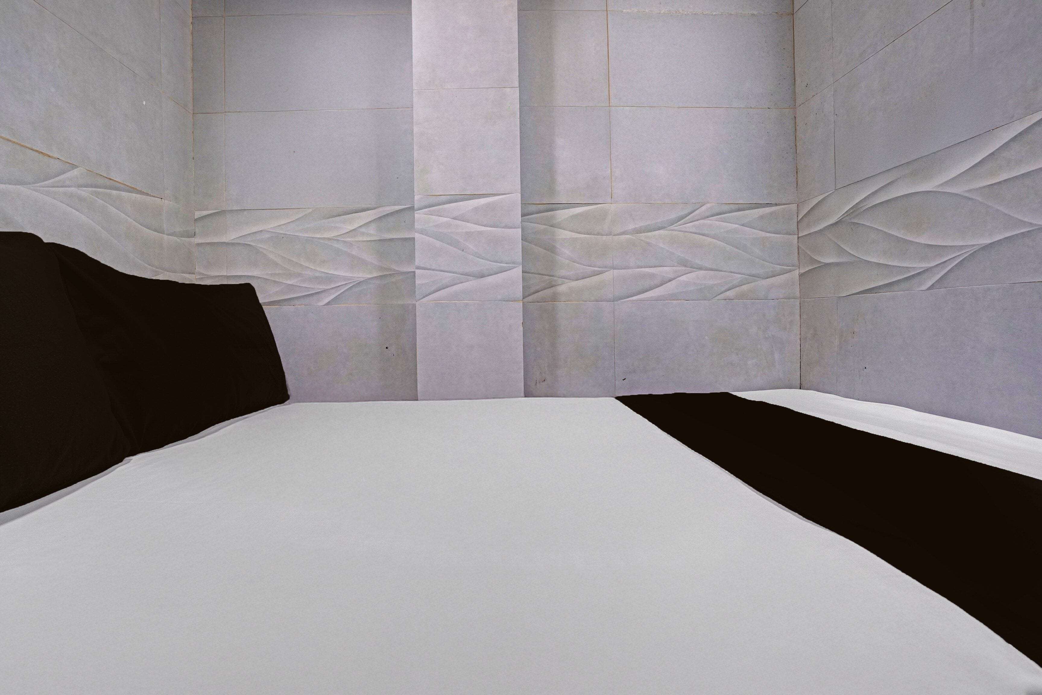 Una habitación con una cama, cabecera negra y un muro con estampado de hojas.