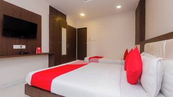 A hotel room with a large bed, a flat-screen TV mounted on the wall, and a wooden headboard.