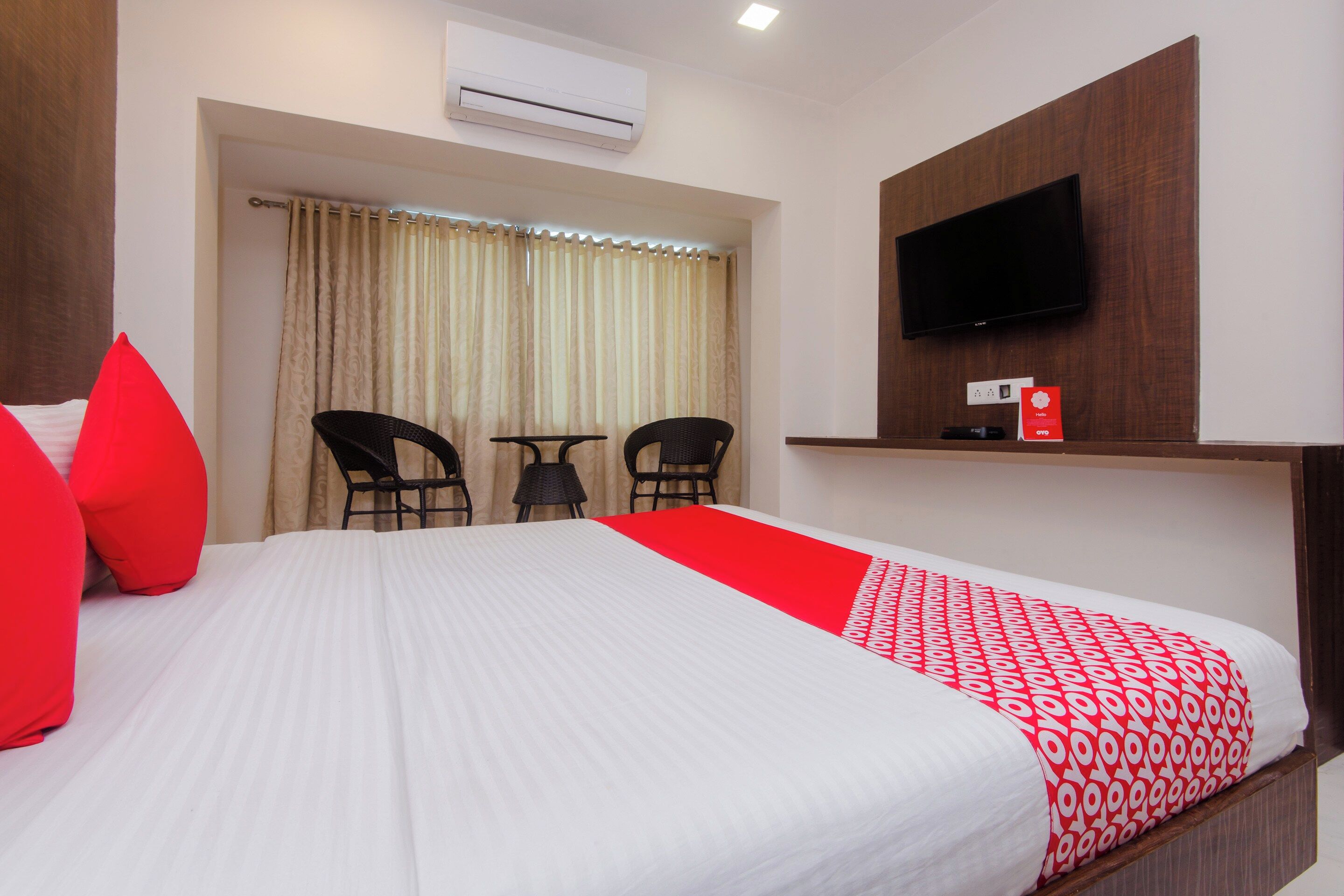 Ein Hotelzimmer mit Bett, Wandfernseher, Schreibtisch mit Stuhl und einem Vorhangfenster.