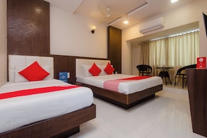 A hotel room with two beds, a ceiling fan, an air conditioning unit, a desk with a chair, and a view of the outside. - Hotel O Alfa Grand (Mumbai)