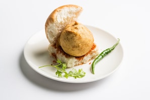 A plate with a bread roll and a ball of food, garnished with green herbs and a chili pepper. - Hotel O Alfa Grand (Mumbai)