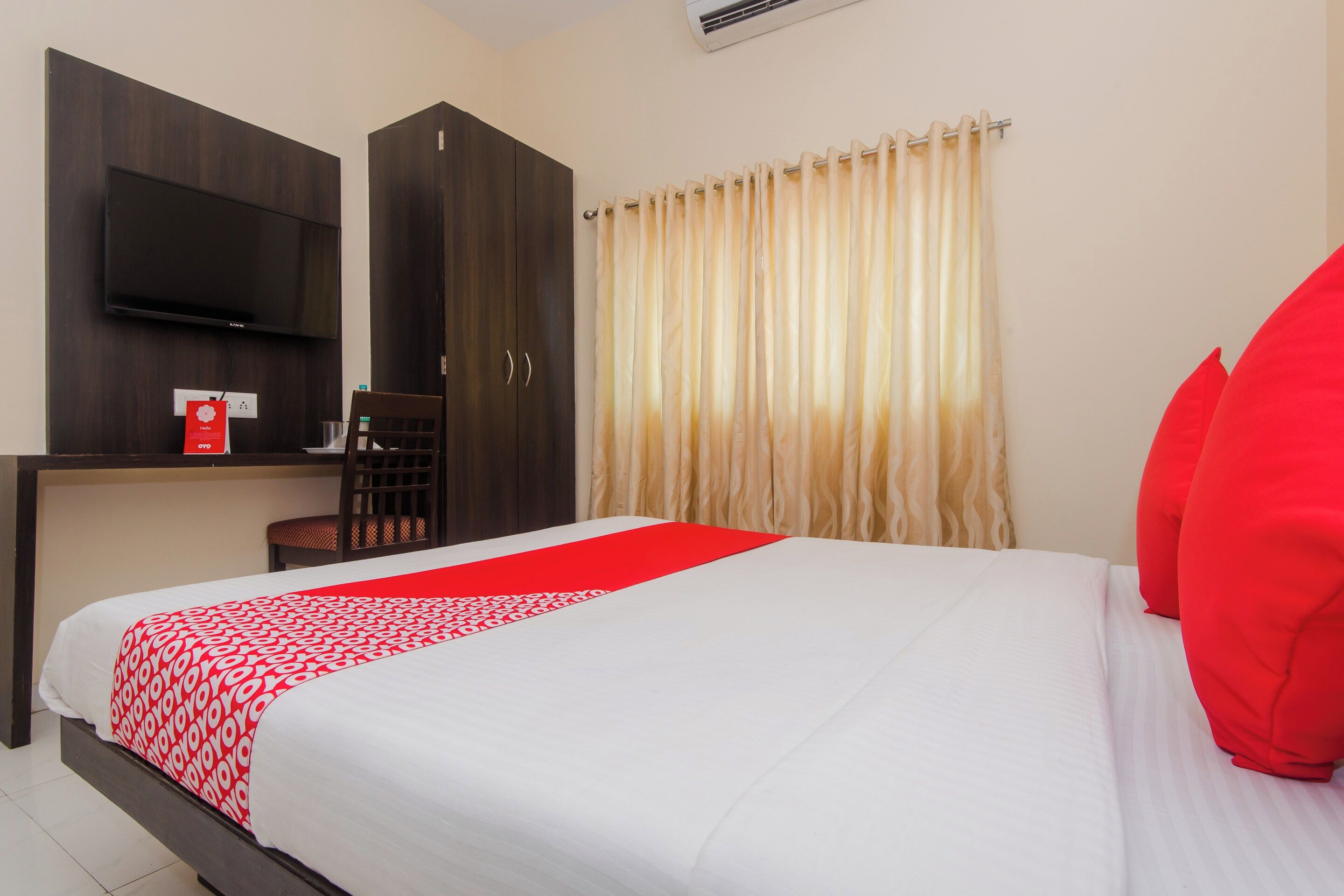 A hotel room with a bed, a desk, a chair, a TV, and a window with curtains.