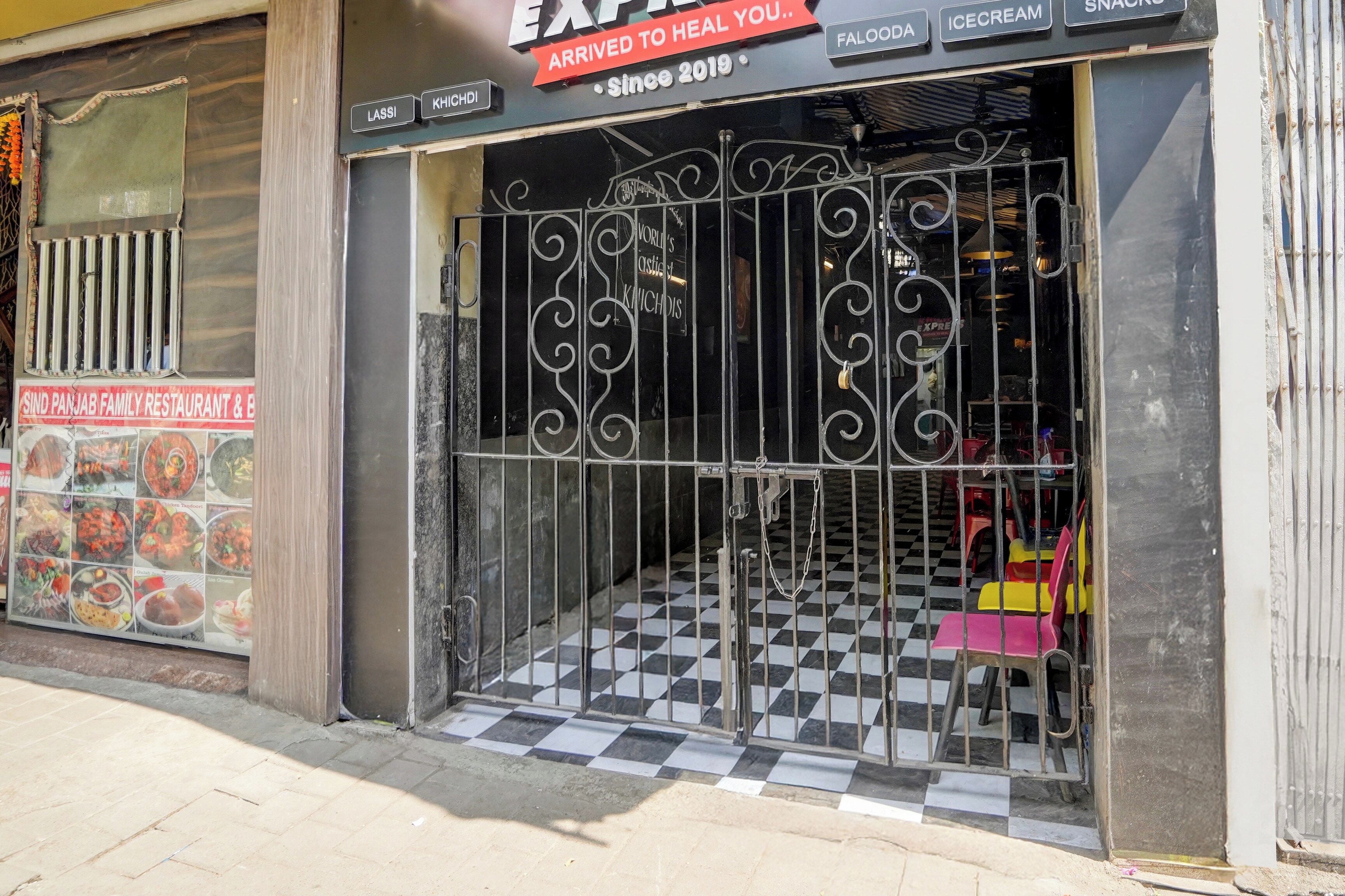 Une devanture de magasin avec un sol à carreaux noirs et blancs, une grille métallique et une enseigne indiquant que l’établissement est en activité depuis 2019.