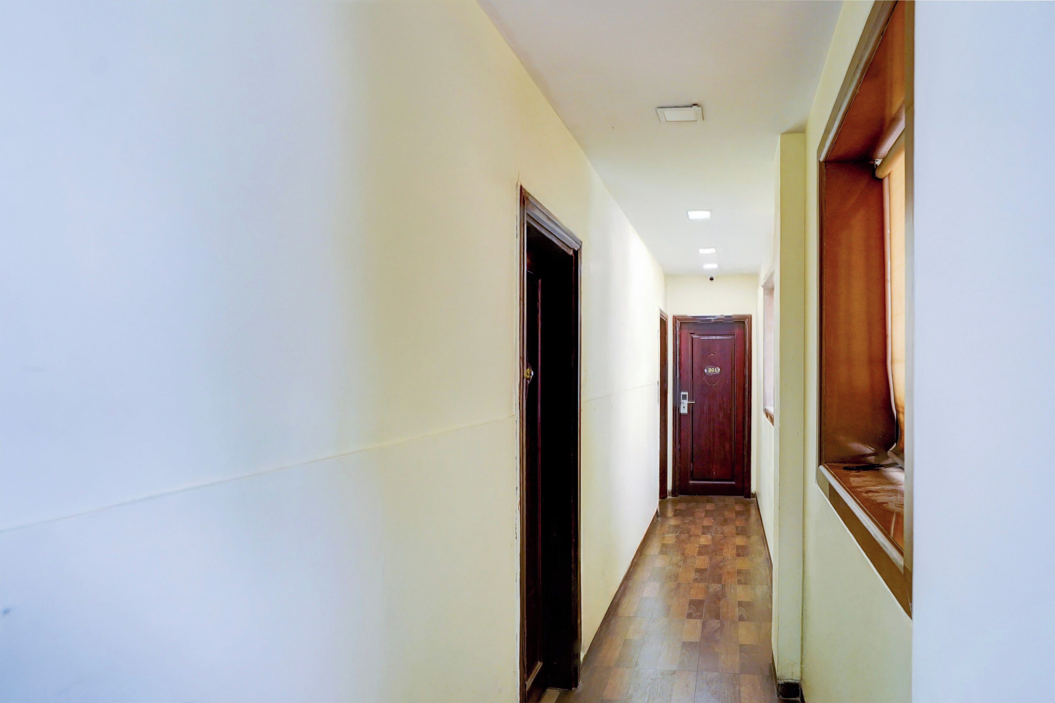Un couloir étroit avec un plancher en bois, une porte avec une plaque numérotée et une fenêtre avec un cadre en bois.