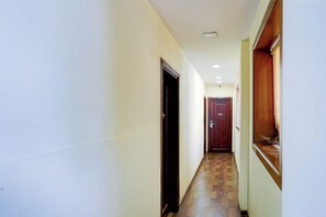 A narrow hallway with a wooden floor, a door with a number plate, and a window with a wooden frame.