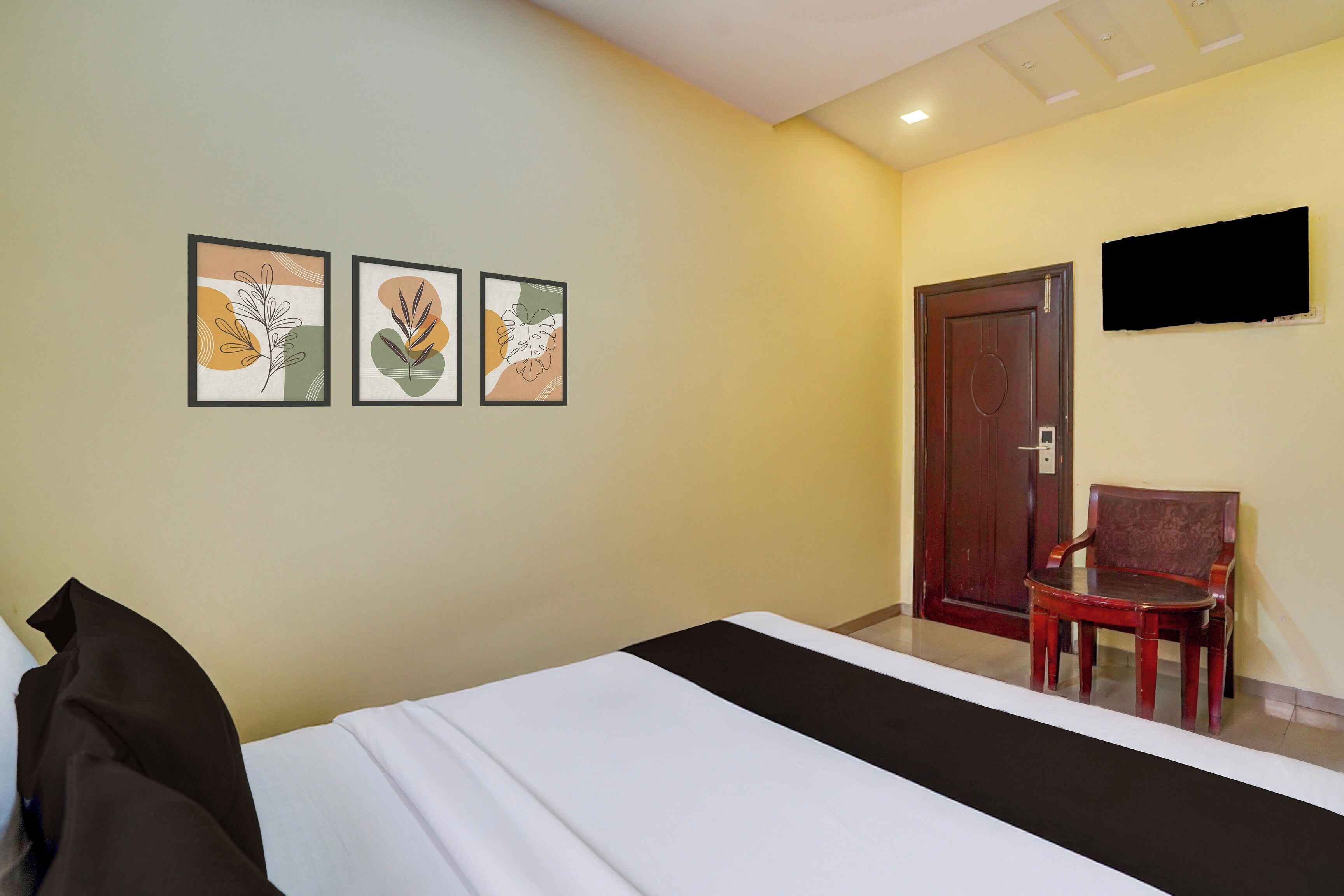Une chambre d’hôtel avec un lit, une chaise, un téléviseur fixé au mur et trois œuvres d’art encadrées accrochées au mur.