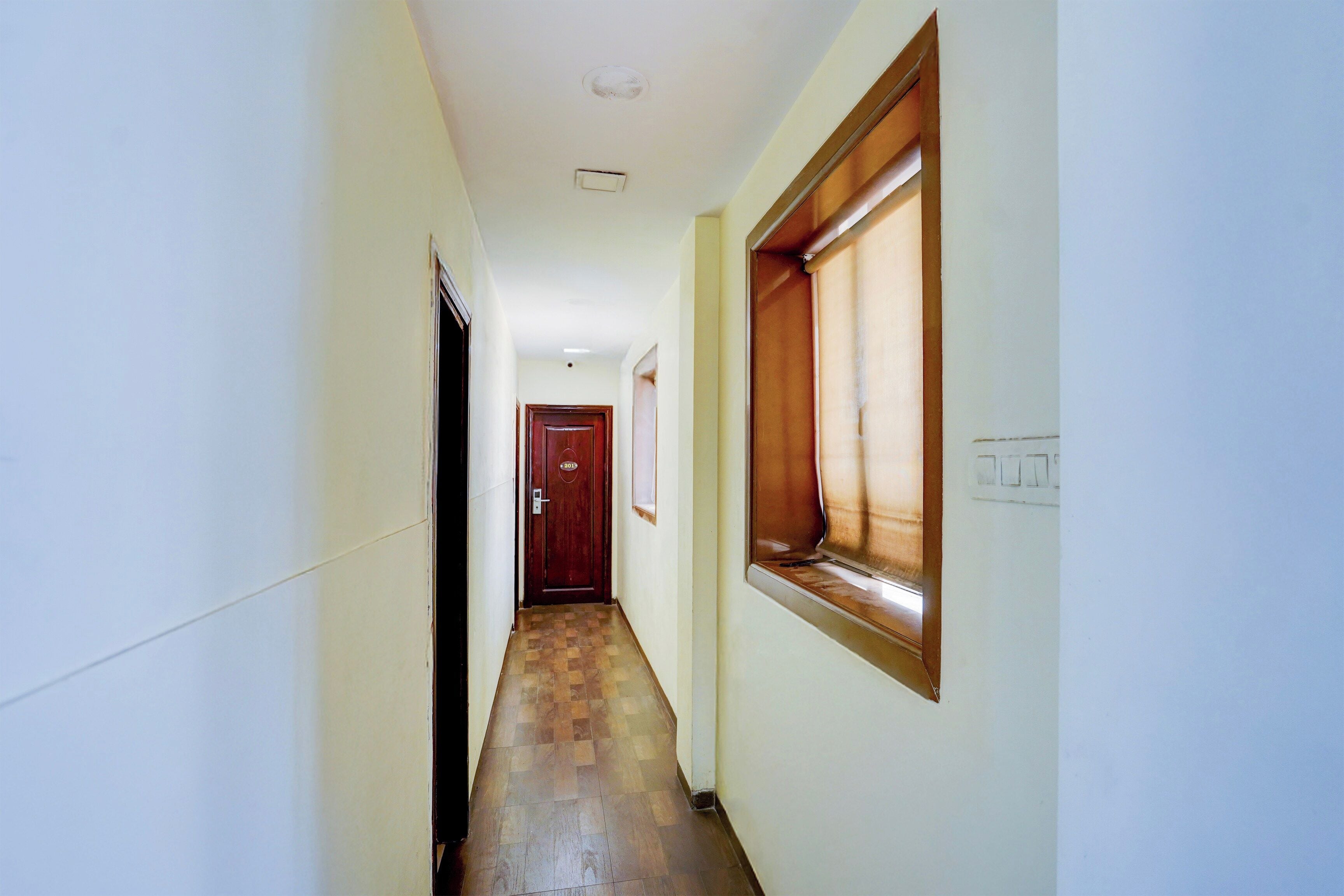 Un couloir étroit avec un plancher en bois, une porte au fond et une fenêtre sur le mur de droite.