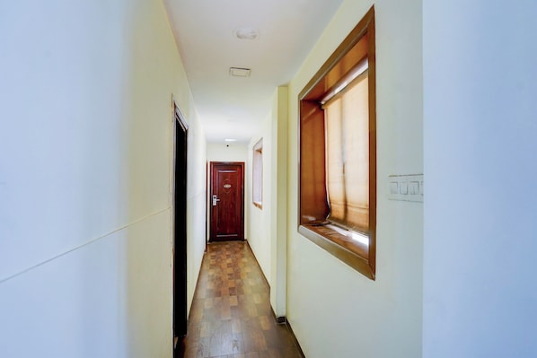A narrow hallway with a wooden floor, a door at the end, and a window on the right wall.