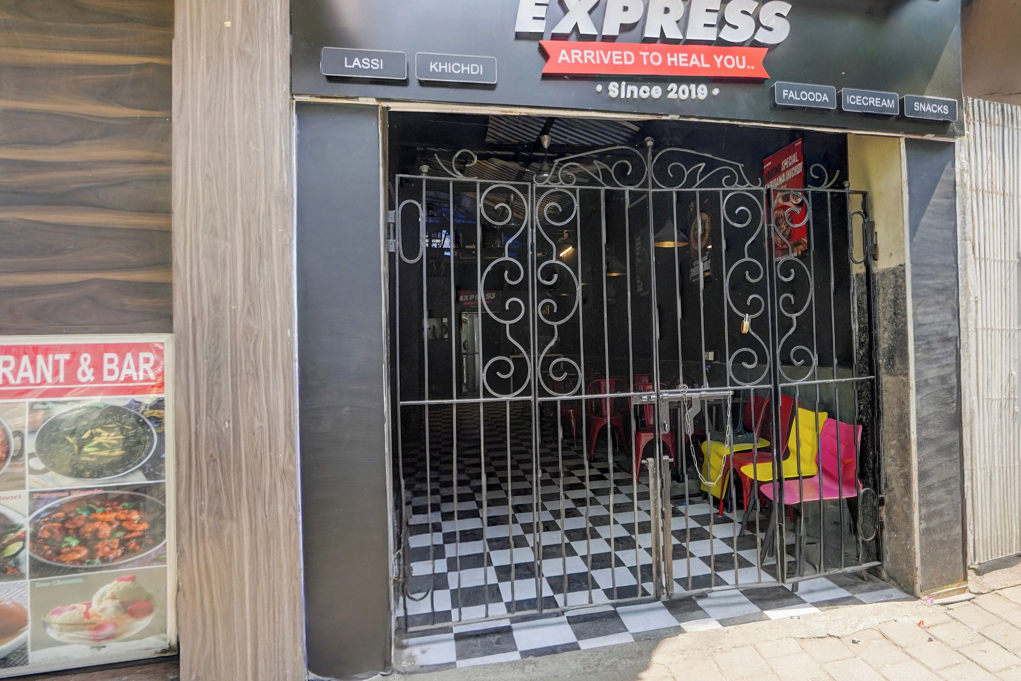 L’entrée d’un restaurant avec un sol à carreaux noirs et blancs, un portail en métal et une enseigne au-dessus indiquant : « EXPRESS, À VOTRE SERVICE POUR VOUS OFFRIR UN MOMENT DE DÉTENTE… Depuis 2019 ».