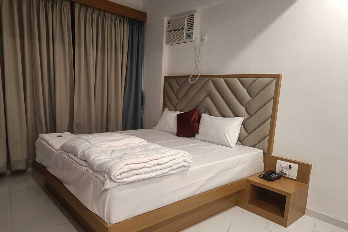 A hotel room with a bed, a bedside table with a phone, and a wall-mounted air conditioning unit.