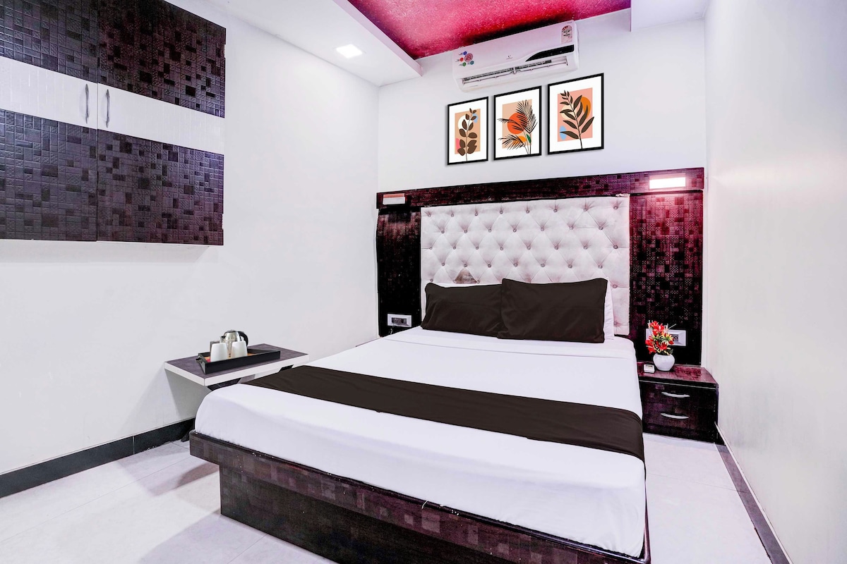 A modern bedroom with a large bed, a nightstand, a wall-mounted air conditioner, and framed artwork.