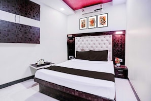 A modern bedroom with a large bed, a nightstand, a wall-mounted air conditioner, and framed artwork. - Townhouse Asalpha Near International (Mumbai)
