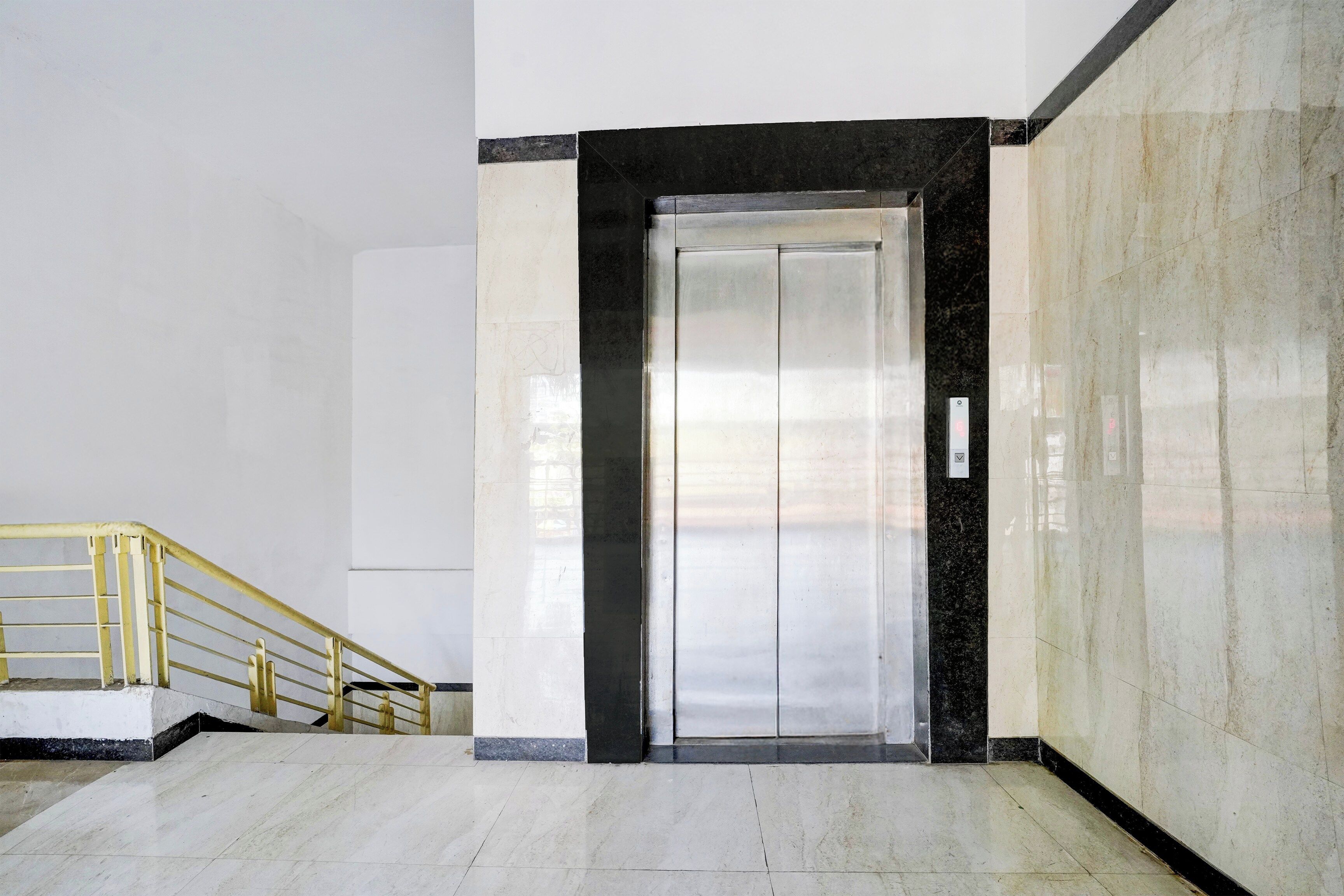 A clean, modern elevator with a metallic finish, flanked by white walls and a marble floor.