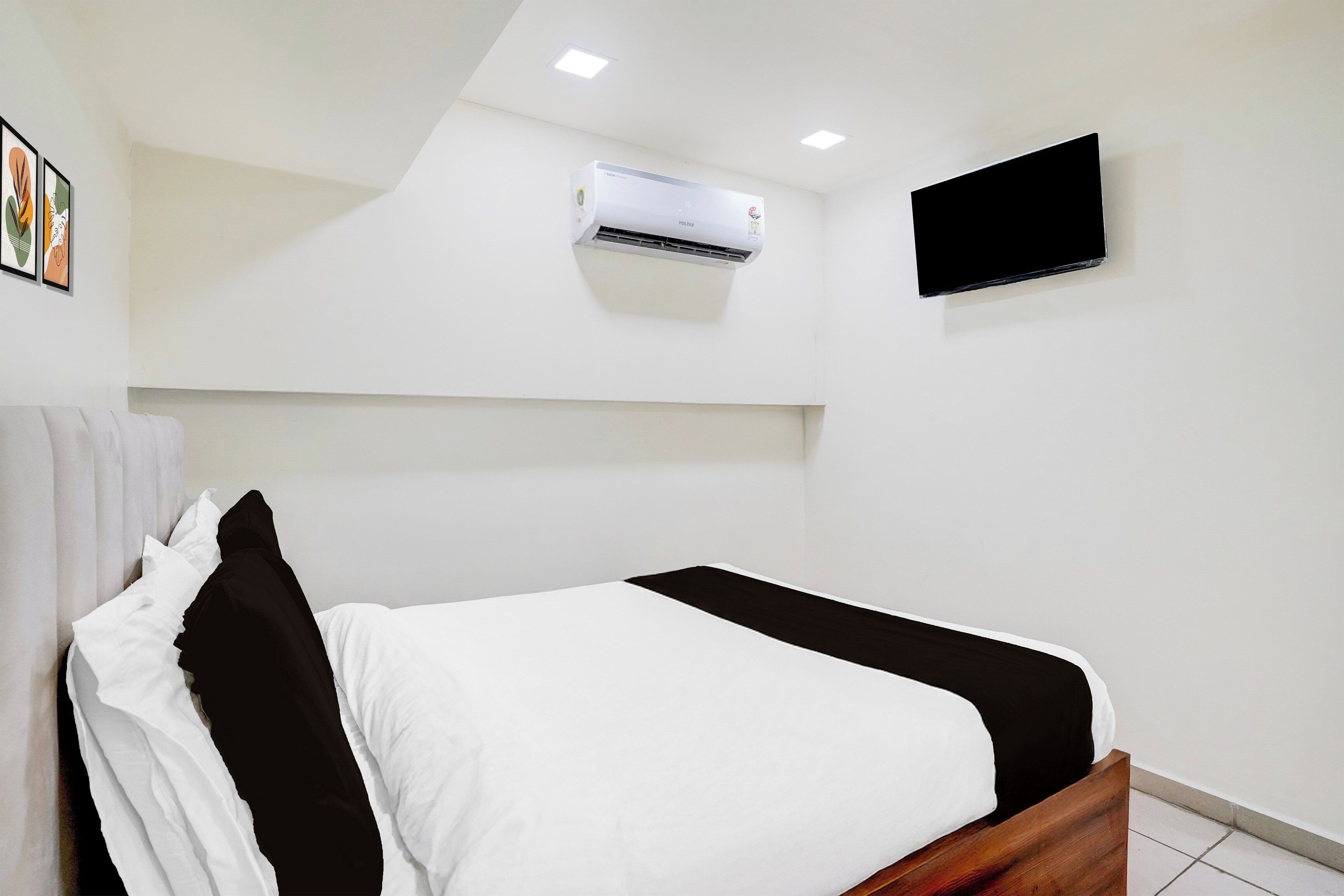 A hotel room with a bed, a mounted air conditioner, a flat-screen TV, and a ceiling light.