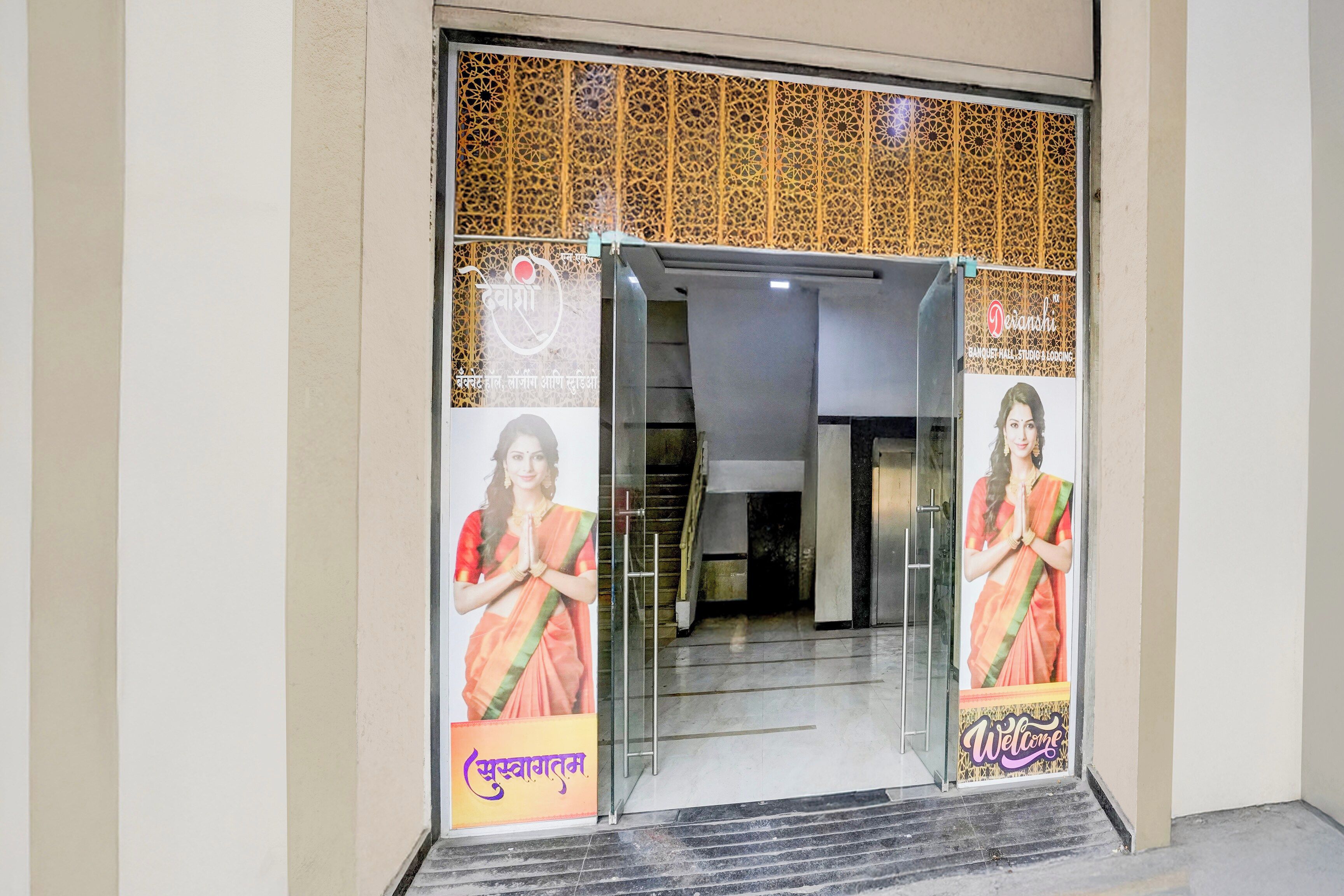 A hotel entrance with a glass door, a patterned wall, and a welcome sign.