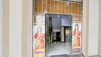 Entrada de hotel con puerta de vidrio, pared con diseño y cartel de bienvenida.